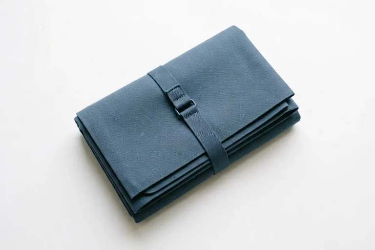 A folded slate-blue travel yoga mat with a slim carry strap on a white surface, showing the easy packing of the best travel yoga mats.