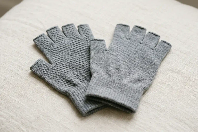 A pair of fingerless gray yoga gloves with silicone grip dots laid out on a light surface, among the best yoga gloves for better hand stability.
