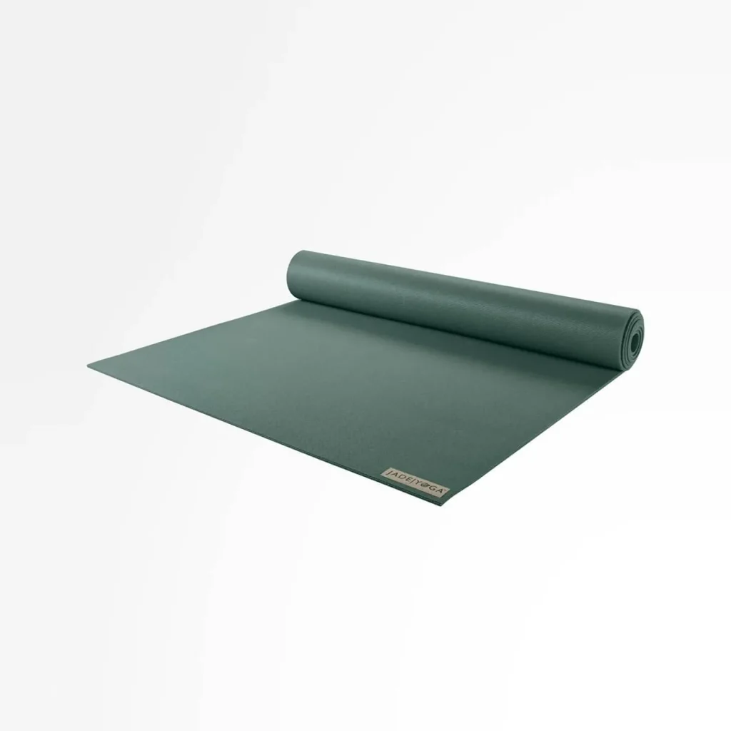 The JadeYoga Harmony natural rubber mat in deep green lies folded with its rolled form resting behind it. 8 Best Natural Rubber Yoga Mats for Yogis Who Want Dense Cushioning and Reliable Traction