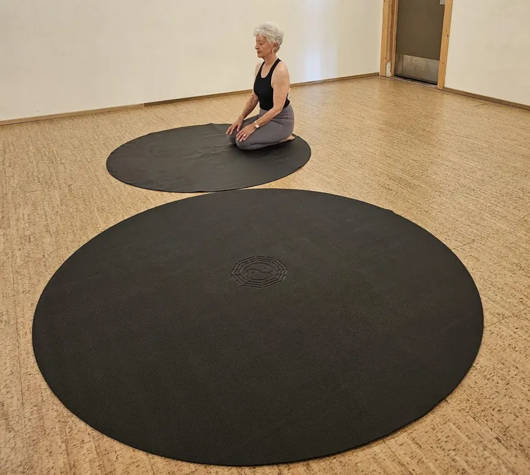 Black circular mat with embossed yin-yang circle centered in a wooden studio.