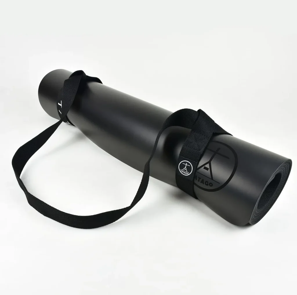 The Tatago Carbonegro natural rubber mat rests rolled with its carry strap buckled around it.