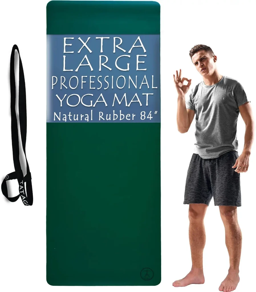 The Tatago natural rubber hot yoga mat in emerald rests rolled with its carry strap looped around it.